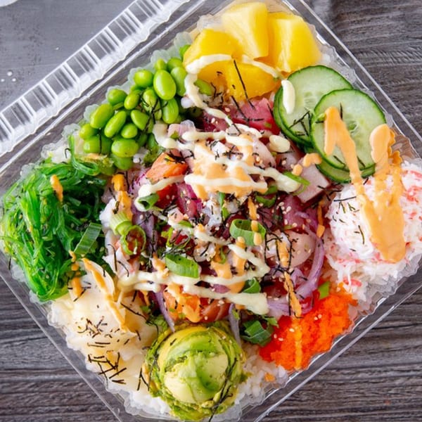 Colorful Poke Rainbow bowl with tuna, salmon, avocado, edamame, pineapple, and various toppings.