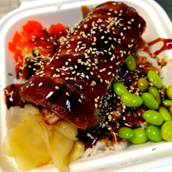 Poke bowl with eel, sesame seeds, edamame, and roe in a white container.