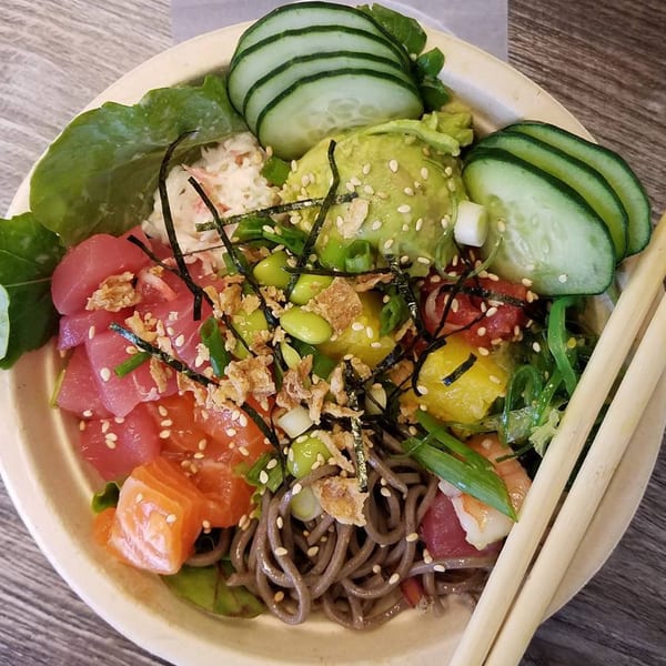 A vibrant poke bowl with tuna, salmon, avocado, cucumber, edamame, and soba noodles.