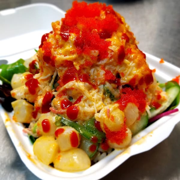 Poke Rainbow's poke bowl with scallops, green vegetables, and red roe in a white takeout container.